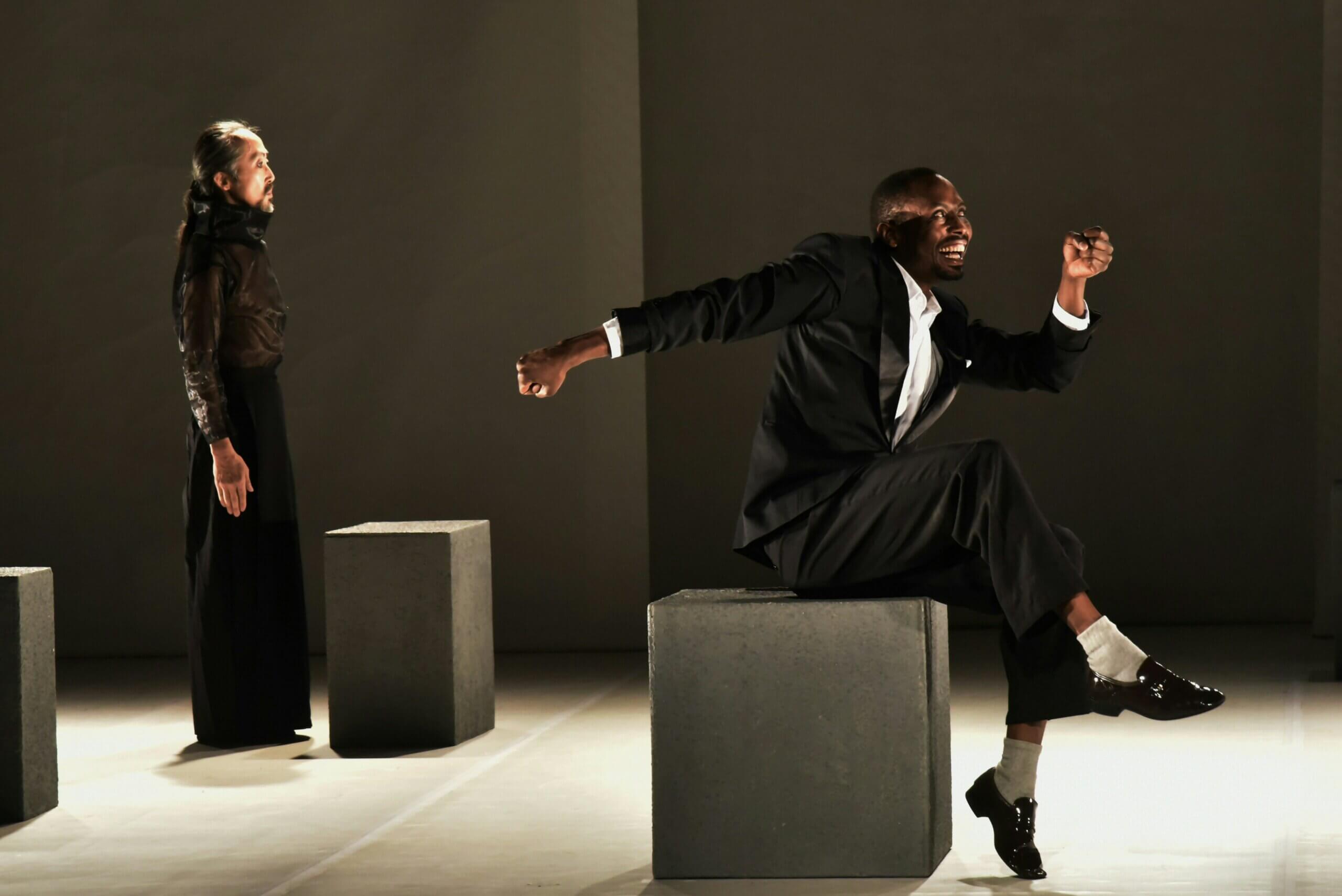 African actor in a suit and Asian actor in a robe and jacket performing.