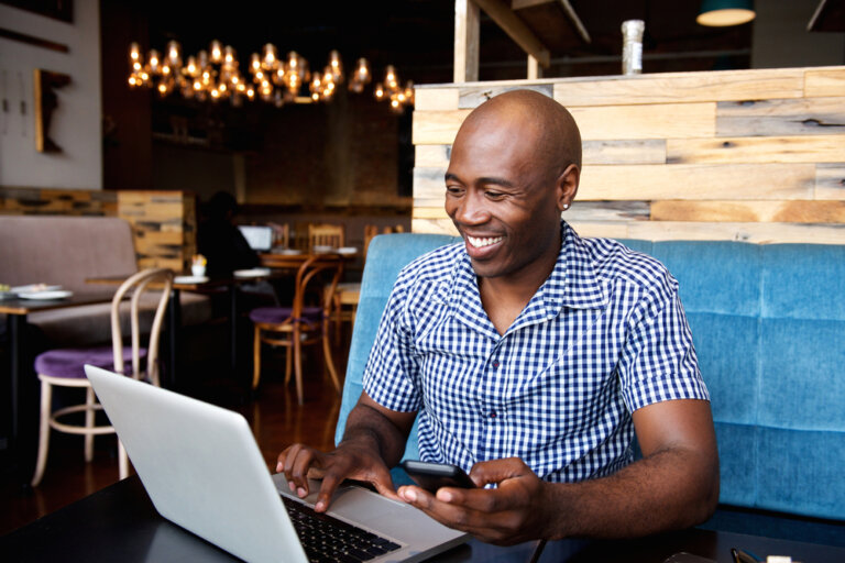 Happy bald man in a blue shirt on his laptop in a restaurant.