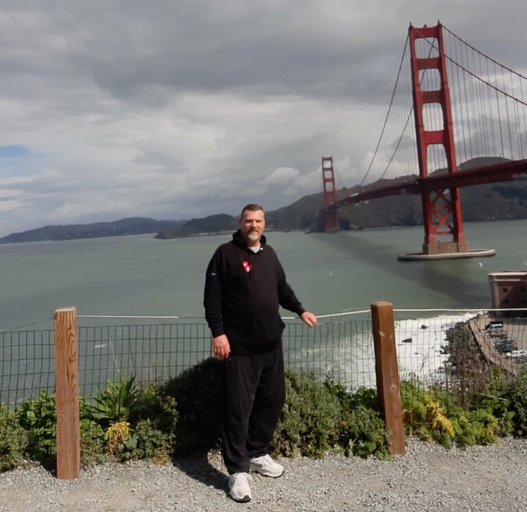 Tim Swain in a track suit smiling by the Golden Gate Bridge.