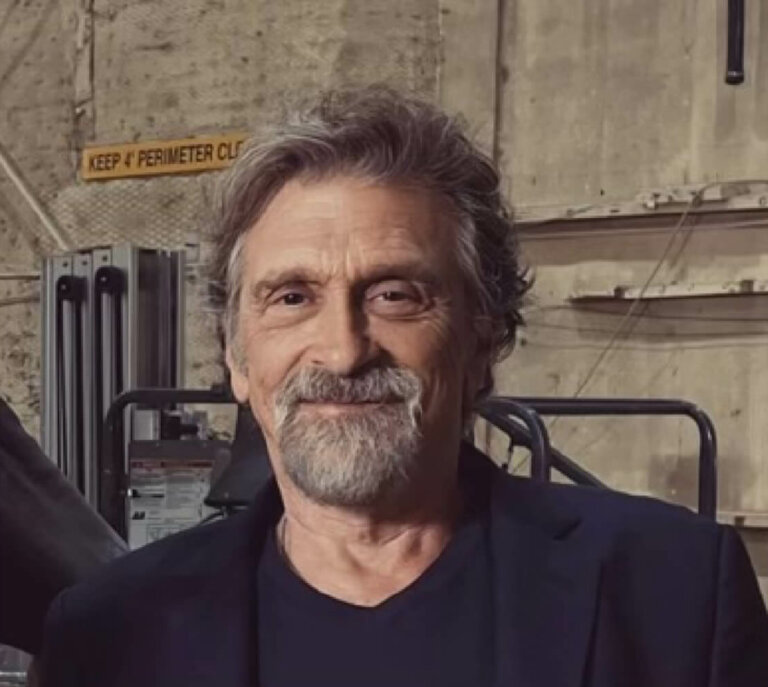 Dennis Boutsikaris in front of a concrete backdrop smiling.