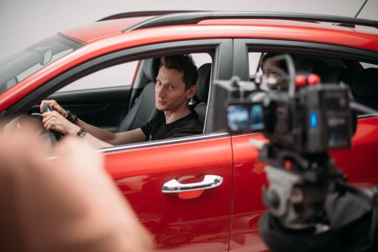 Actor in a red car filming a commercial.