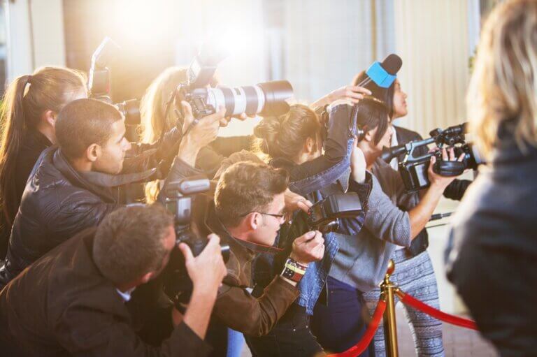 Paparazzi photographers at a red carpet events taking pictures of a famous person.
