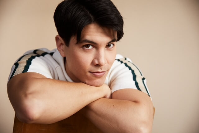 Actor James Phoon sitting in a chair, arms crossed and smiling.