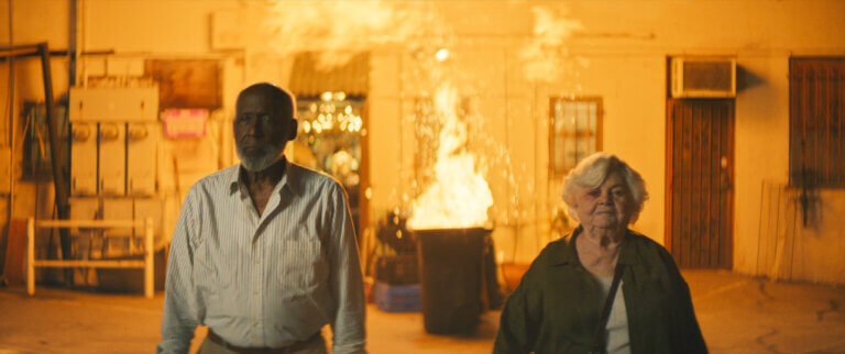 June Squibb and Richard Roundtree walking away from a burning garbage can inside.