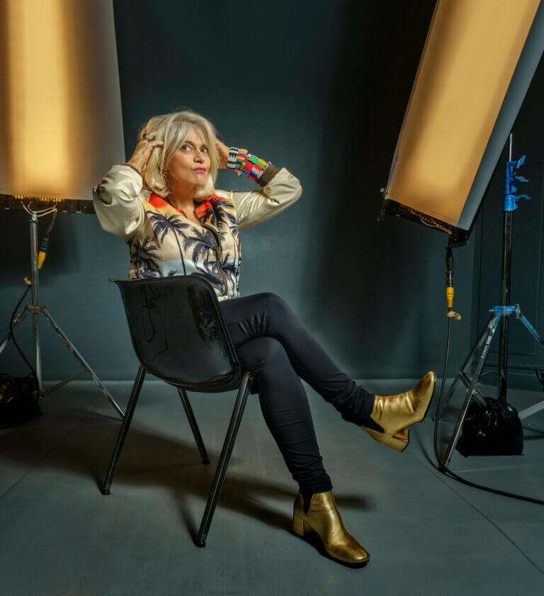 Juliette Ménager sitting in a chair inside a dark studio, hands in hair.