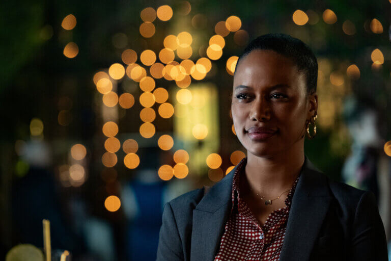 Taylour Paige in a suit at night looking suspicious at someone.
