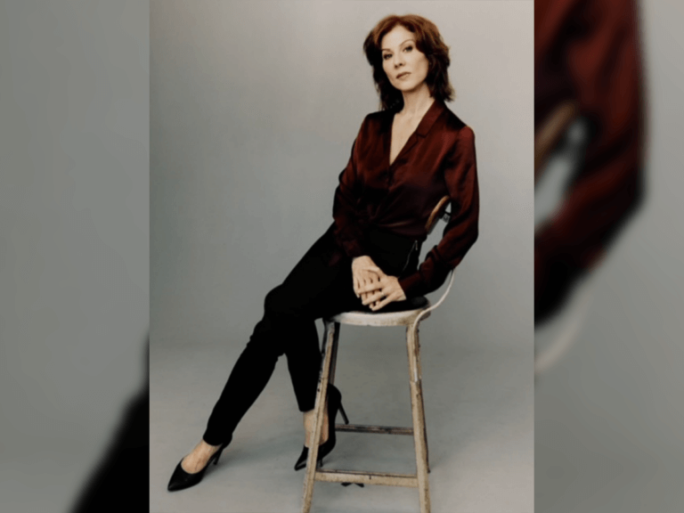 Stephanie Kurtzuba in a red dress shirt sitting asymmetrical on a chair.