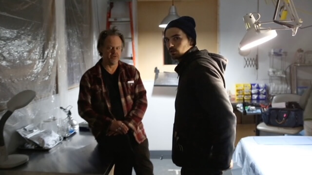 Chris Skothdople and Larry Fessenden chatting in a dimly lit room.
