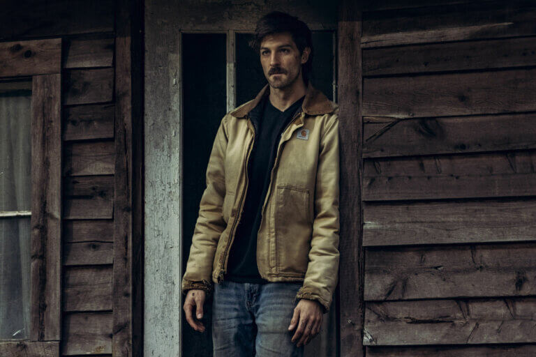 Jake Allyn standing outside a cabin with a tan jacket on.