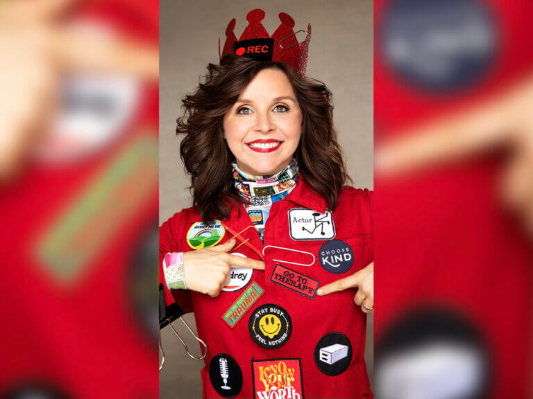 Audrey Helps Actors host Audrey Moore wearing a crown and shirt with patches smiling and pointing to a patch.