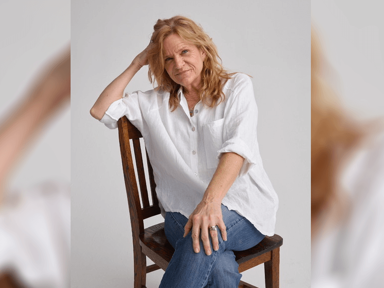 Dale Dickey sitting in a wooden chair in a gray room smiling.