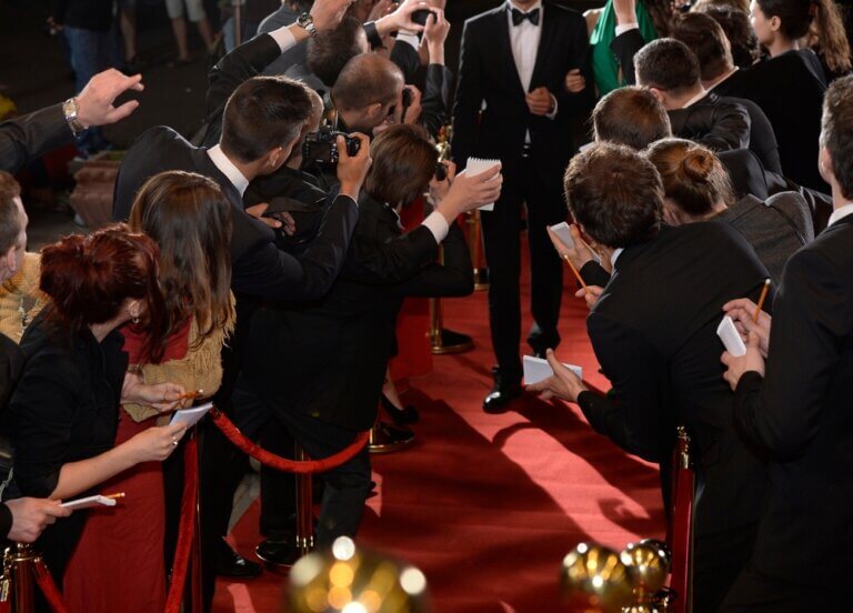 Actor on a red carpet with paparazzi taking pictures.