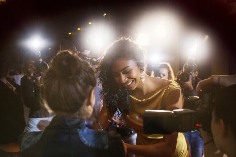 Female celebrity in a gold dress signing autographs at a red carpet event.