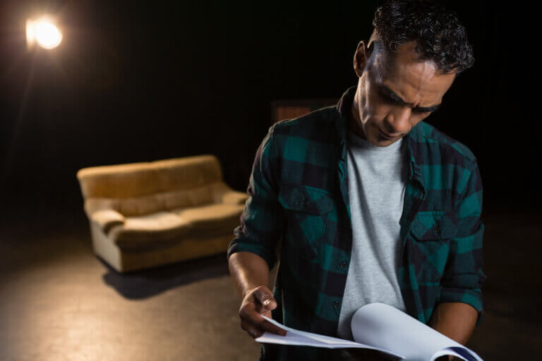 Actor on a stage before a couch reviewing the script.