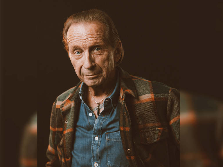 Paul Raci wearing flannel and smiling.