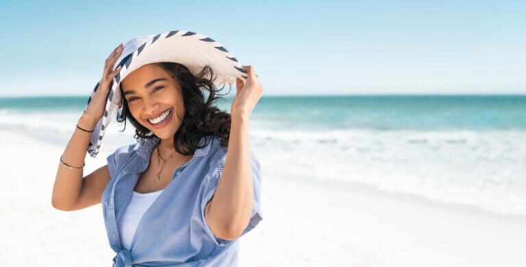 Happy Spanish woman on the beach with a sun hat and blue shirt.