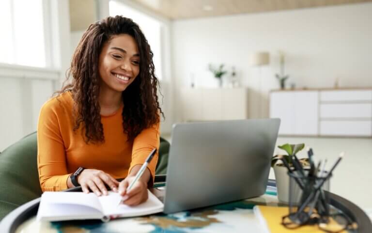 Happy Black woman at home working and taking notes.