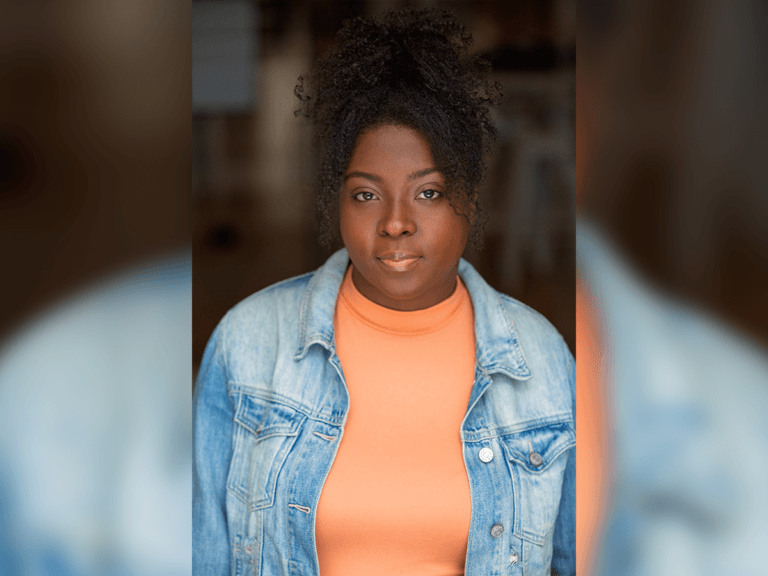 Umia-Jones Watson smiling in a denim jacket and orange shirt.