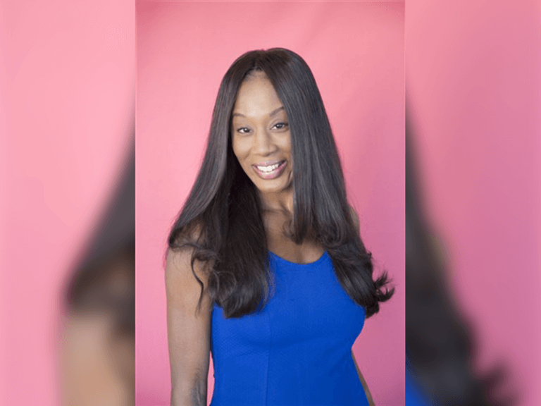 Actress Lana Leigh Taylor smiling in a blue shirt with a pink backdrop behind her.