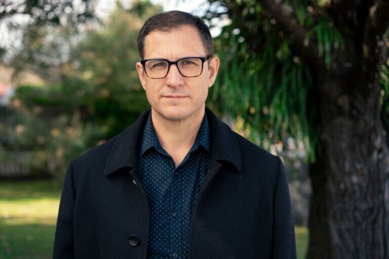 Casting Director Peter Rasmussen in a black jacket and blue shirt standing by a tree in a park.