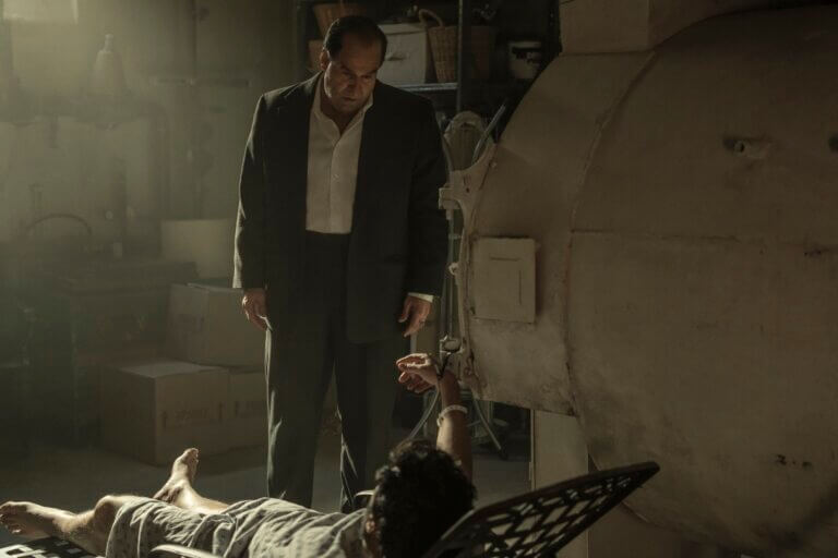 Colin Ferrell as "The Penguin" looking menacing over a victim in a concrete basement.