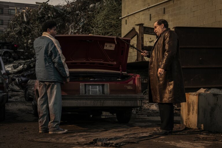 Colin Ferrell as "The Penguin" in front of a car with an open trunk in an alley.