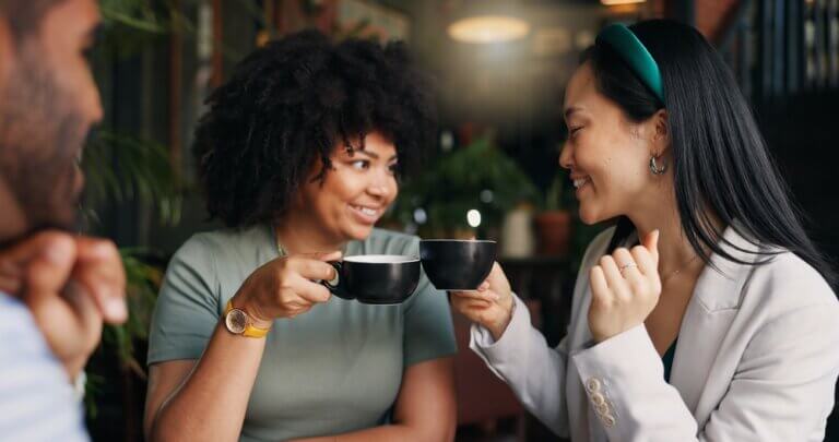 Three friends sitting in a coffee shop toasting.