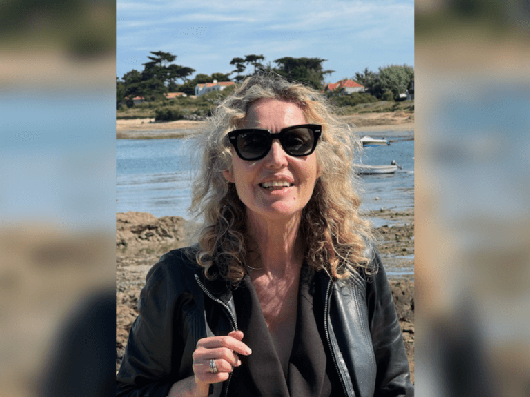 Casting Director Caroline Sinclair smiling on the bank of a river in a leather jacket.