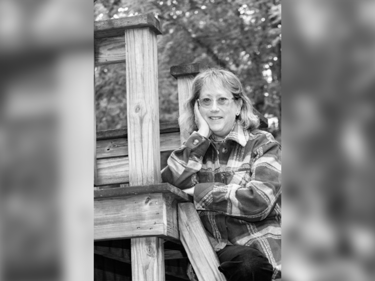 Black and white photo of casting director-turned-director Heidi Levitt sitting by a treehouse smiling.