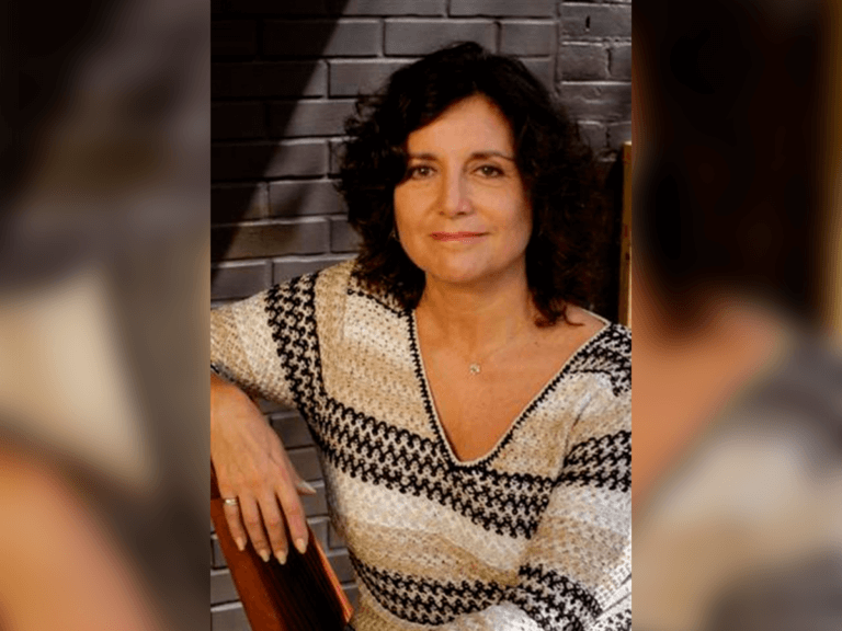 Casting Director Marsha Chesley sitting on a chair in a black, white and gold sweater smiling.