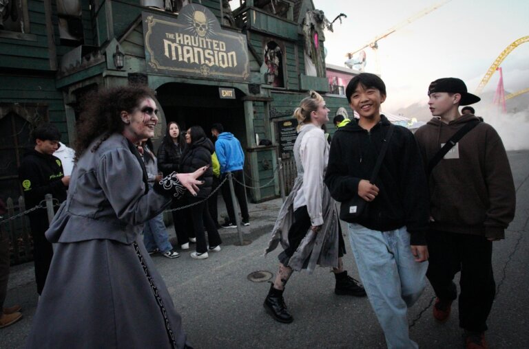 Scare actor dressed as a witch terrorizing theme park guests outside a haunted house attraction.