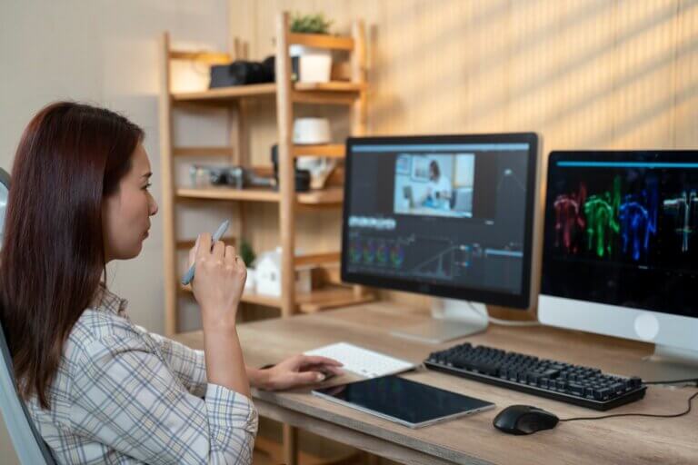 Female Asian actor editing her showreel using two computer monitors at home.