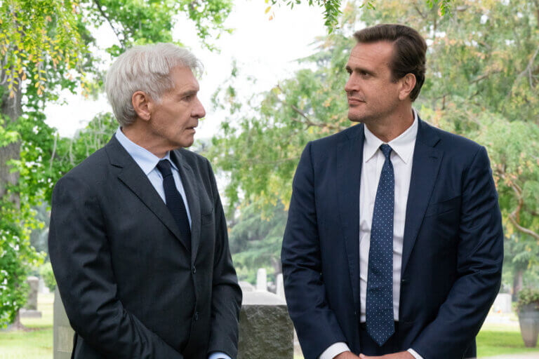 Harrison Ford and Jason Segel at a graveyard in suits.
