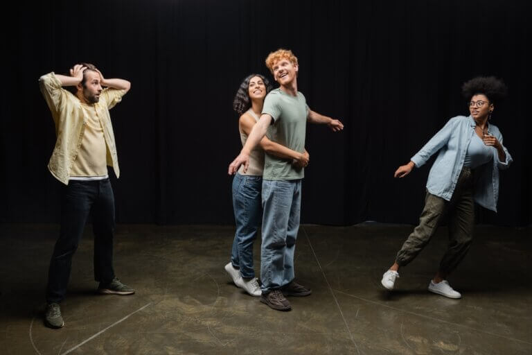 Four diverse actors running through a scene in rehearsal. Two look surprised while two are embracing.