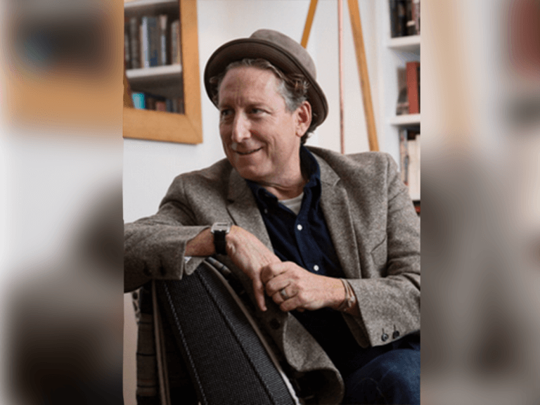 Bernard Telsey sitting in his office in a gray jacket and hat.