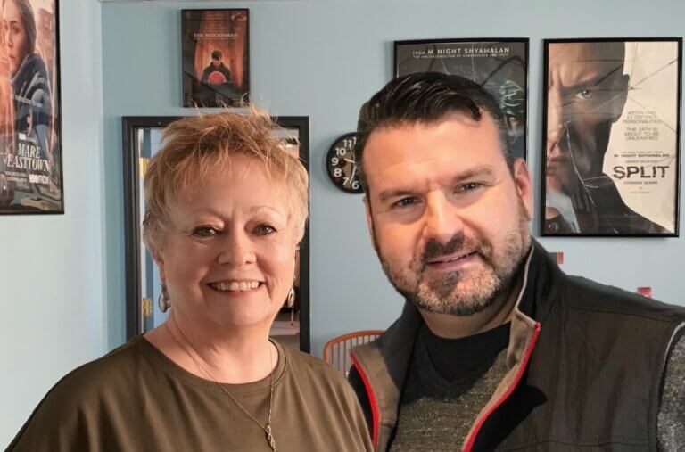Casting director team Diane Heery and Jason Loftus smiling in their office surrounded by movie posters.