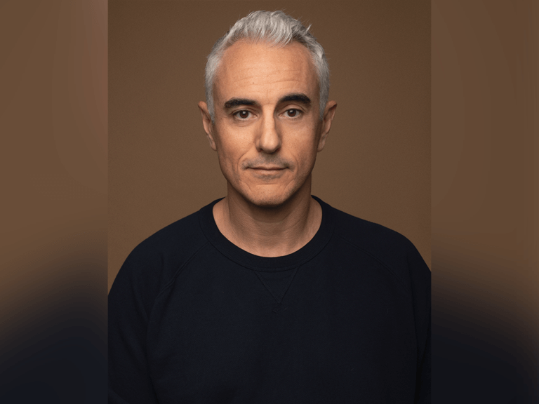 Actor Oliver Vaquer smiling in a black sweater.