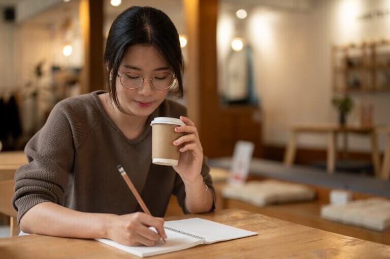 Asian woman at a coffee shop, latte in hand, making a list.