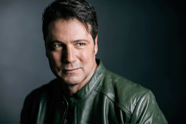 Actor/Casting Director Jayson Therrien smiling in a dark room wearing a leather jacket.