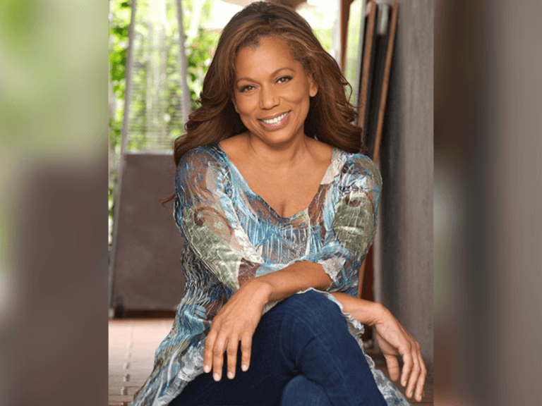 Rolonda Watts sitting on a couch indoors wearing a floral shirt and blue jeans.
