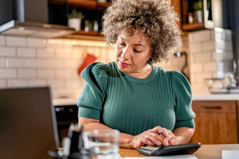 Middle-aged woman crunching numbers and budgeting at her kitchen table.