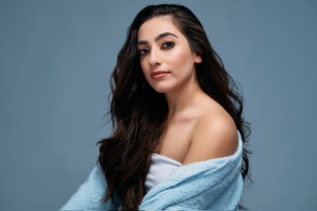 Actress Amber Afzali in a blue cardigan, white shirt smiling.