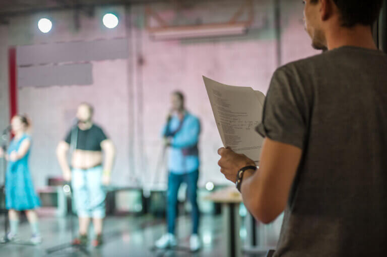 Actor, script in-hand, walking into a callback audition. Several other actors are waiting in a lineup.