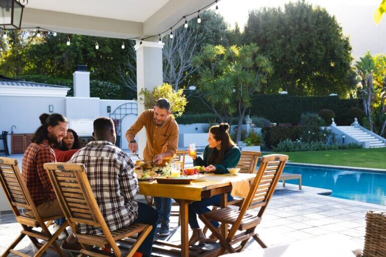 Happy diverse group of friends enjoying a healthy breakfast by a beautiful luxrious mansion pool and backyard.