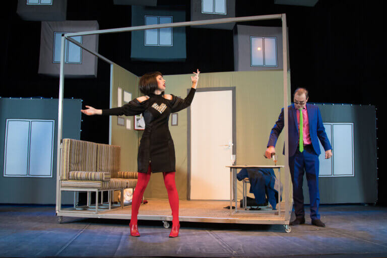 A woman and man performing a farce play onstage with a fake set.