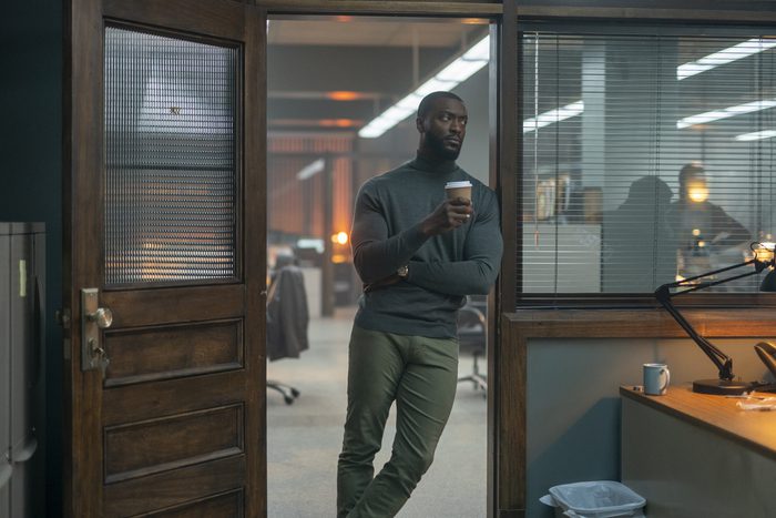 Aldis Hodge as Alex Cross leaning on the open door of a detective's office holding a cup of coffee.