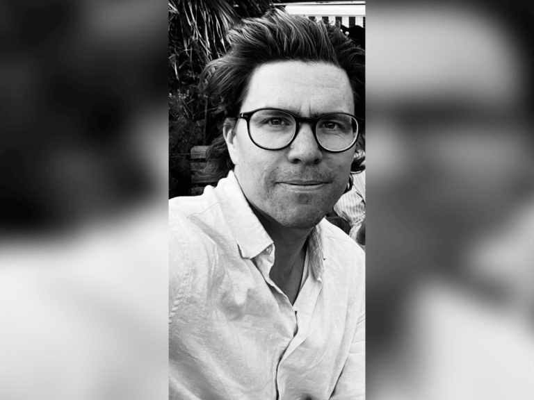 Black and white filtered image of Casting Director Finnian Tweed smiling outside.