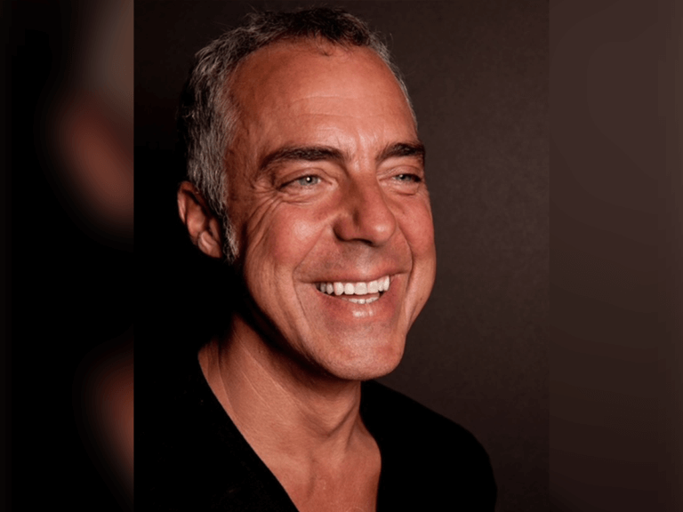 Actor Titus Welliver wearing a black shirt and smiling inside.