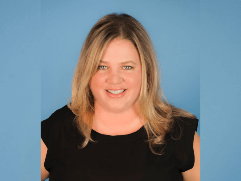 Castign director Wittney Horton smiling in a black shirt on a blue background.