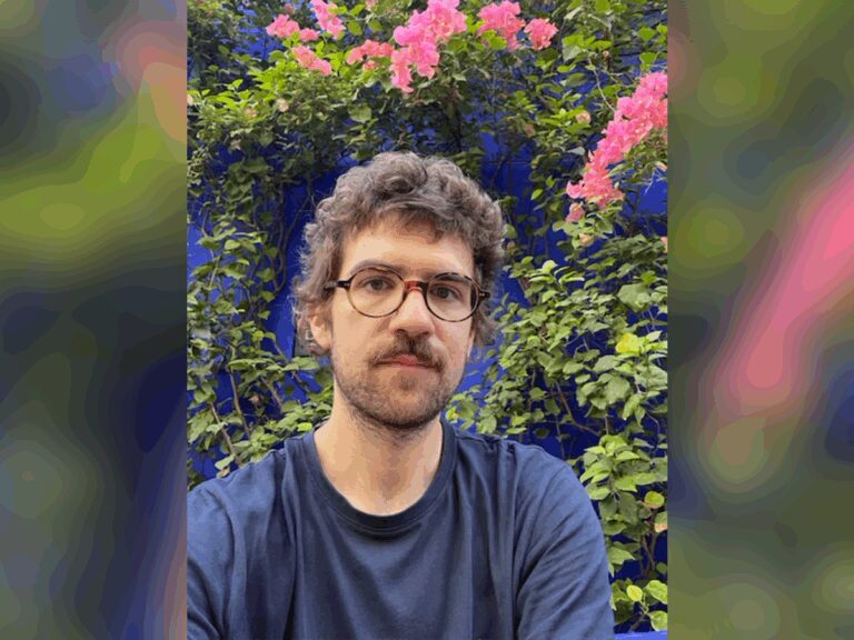 Casting director Alejandro Gil outside a botanical garden with pink blossoms in a blue t-shirt.